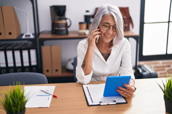 オフィスでタッチパッドを使用してスマートフォンで話している中年の白髪の女性ビジネスワーカー — ストック写真