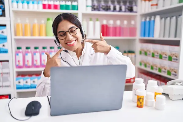 Young arab woman working at pharmacy drugstore using laptop smiling cheerful showing and pointing with fingers teeth and mouth. dental health concept.