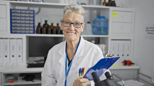 Starsza Kobieta Naukowiec Siwymi Włosami Pewnie Uśmiecha Się Laboratorium Trzymając — Zdjęcie stockowe