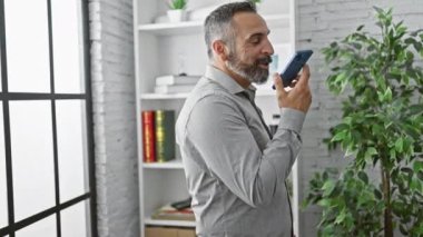 Modern ofiste akıllı telefon kullanan kıdemli İspanyol sakallı adam..