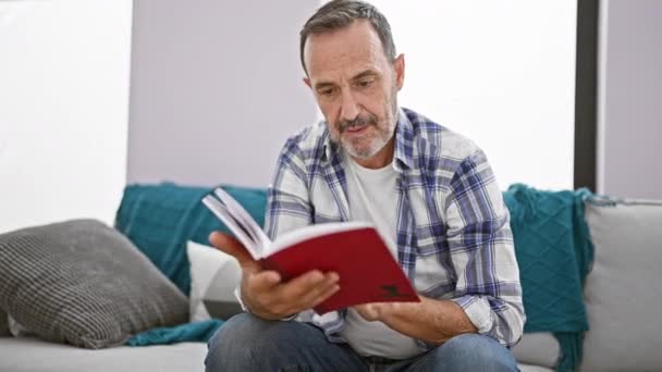 Μεσήλικας Άνδρας Γκρι Μαλλιά Ανάγνωση Βιβλίο Κάθεται Στον Καναπέ Χαμογελώντας — Αρχείο Βίντεο