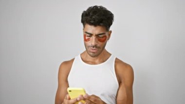 Sakallı genç bir İspanyol, beyaz bir arka plana karşı göz bandı takıp selfie çekiyor..
