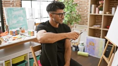 Parlak bir sanat stüdyosunda elinde fırça tutan, gözlüklü ve sakallı yakışıklı bir İspanyol..