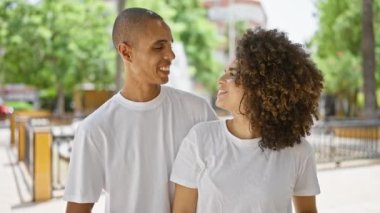 Kendinden emin, mutlu bir çift parkta gündelik bir günün tadını çıkarıyor, güzel bir kucaklaşmayı paylaşıyor, gülümsüyor ve gökyüzünü işaret ediyor..