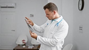Konsantre olmuş beyaz önlüklü erkek doktor modern bir kliniğin muayene odasında röntgen filmini inceliyor..