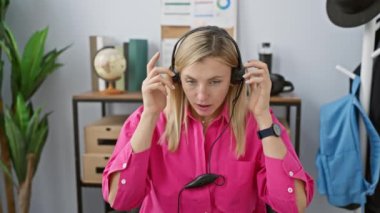 Stresli genç kadın modern ofis ortamında kulaklığı çıkartıyor, hayal kırıklığı ve işyeri yorgunluğu gösteriyor..