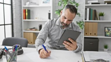 Olgun sakallı adam, ofisinde tablet kullanarak yazıyor.