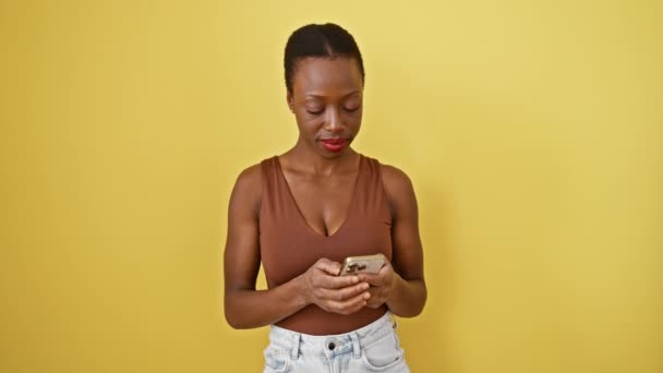 笑顔のアフリカ系アメリカ人女性が携帯電話を持ちながら Okay のサインを撮り 黄色い隔離された背景に優れたテキストの上に幸せを表現します — ストック動画