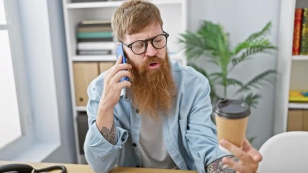 若くてハンサムで赤毛のビジネスマンがスマートフォンで真剣に話し オフィスでエスプレッソコーヒーを飲んで集中を表現する屋内で座って — ストック動画