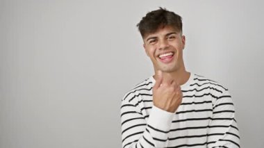 Çizgili, neşeli, genç, İspanyol bir adam baş parmağıyla yan tarafı işaret ediyor! Mutlu ve kendinden emin görünüyor. İzole edilmiş beyaz arka planda gülümsüyor. Reklam için mükemmel.! 