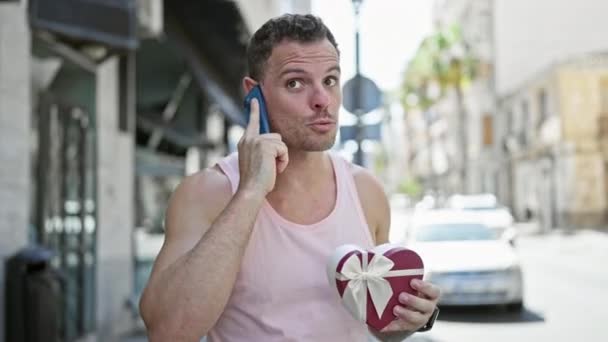 一个英俊的男人拿着礼品盒在阳光灿烂的城市街道上打电话 — 图库视频影像