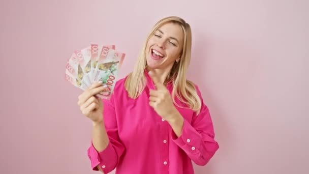 快乐的金发女青年兴奋地指着新的热情和新的美元 对着孤立的粉色背景面带微笑 — 图库视频影像