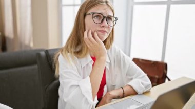 Ofis odasında gözlüklü, laptopla çalışan, odaklanma ya da endişe duygusu taşıyan düşünceli genç bir kadın..