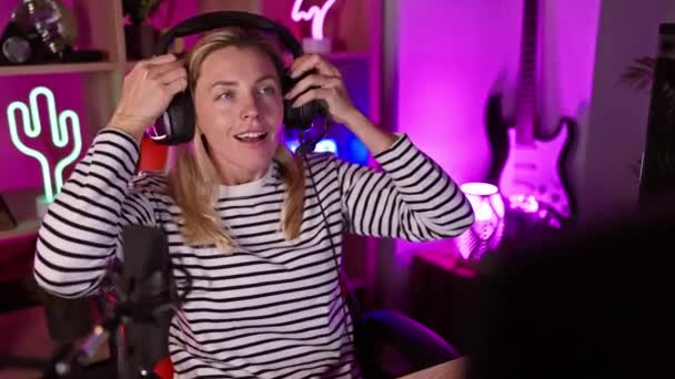 夜のカラフルなゲームルームでヘッドフォンを着用しているブロンドの女性 — ストック動画