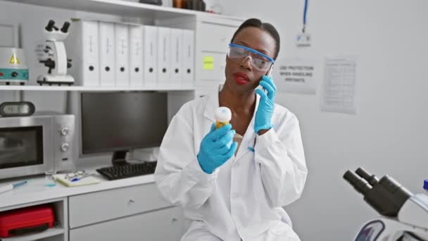 笑顔のアフリカ系アメリカ人女性科学者 研究室で薬をジャグリングしながら 薬局の研究について彼女のスマートフォンで話している — ストック動画