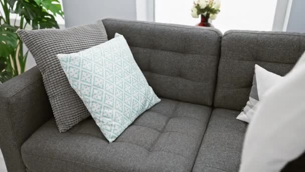 ブロンドの女性は 現代のリビングルームで装飾的な枕と灰色のソファで自宅でリラックス — ストック動画