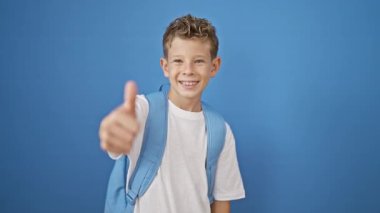 Sevimli, sarışın bir çocuk mavi izole bir arka plana karşı duruyor, gülümserken kendine güvenen bir baş parmak hareketi yapıyor. Küçük, mutlu, zeki bir çocuk çalışmaktan zevk alıyor.!