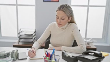 Sarışın güzel sevinçle ışıldıyor, ofis masasında oturuyor, güzel işaret hareketleriyle mükemmel reyting veriyor.