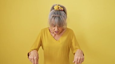 Sarı arka planda at kuyruklu gri saçlı orta yaşlı bir kadın. Heyecan verici bir şekilde bir ilan veriyor, şaşırmış yüzü gerçekten şaşırmış görünüyor..