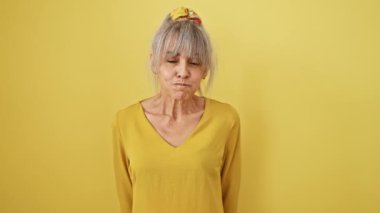 Komik orta yaşlı, at kuyruklu, komik bir yüz takınan, sarı izole edilmiş arka planda, yanakları şişirerek komik bir orta yaşlı kadın.