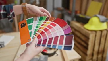 Bir kadın atölye ortamında bir boya örneği seçer, bir iç tasarım projesi için seçenekler sunar.