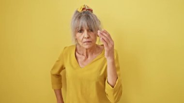 Yorgun, orta yaşlı, at kuyruklu gri saçlı bir kadın yüzünün yarısını uykuyla kapatıyor. Yorgun gözler ve ağız, parlak sarı izole bir arka plana bakıyor..