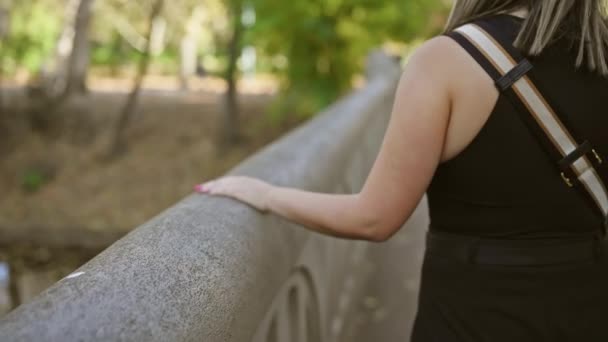 シックな黒いドレスを着た若い女性は 穏やかな秋の公園で雨が降っている橋の上に彼女の手を置く — ストック動画