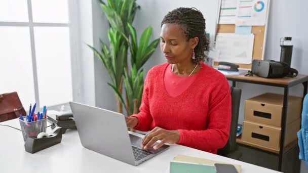 身穿红色毛衣的成熟的非洲女人坐在写字台前沉思 写字台上装有笔记本电脑和文具 — 图库视频影像