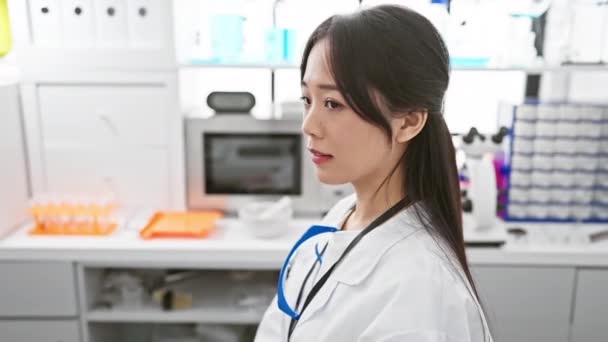 自信に満ちた笑顔は 若い中国の女性科学者 彼女の白い実験室のコートで 研究室の中心に自然の美しさを明らかにする側面のプロフィールを恵みます — ストック動画