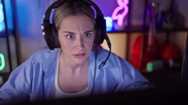 Kulaklık takan odaklanmış genç bir kadın gece renkli neon ışıklı bir oyun odasında oturur ve yoğun bir konsantrasyon ve eğlence duygusunu canlandırır..