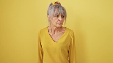 Şaşırmış orta yaşlı, at kuyruklu gri saçlı, elleri başının üstünde, ağzı açık bir kadın. Sarı arka planda izole edilmiş korkmuş, çılgın bir ifade..