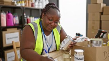 Gülümseyen Afrikalı Amerikalı kadın gönüllü olarak bağışlanan ürünleri kontrol ediyor, sosyal yardım merkezinde notlar alıyor.