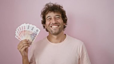 Kıvırcık saçlı neşeli bir genç adam elinde pembe arka planda İzlanda Krona banknotları tutarken gülümsüyor..