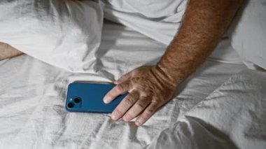 Yorgun, orta yaşlı, beyaz sakallı bir adam rahat bir şekilde battaniyenin altına kıvrılıyor, derin bir uykuya dalıyor ve elinde bir akıllı telefon tutuyor..