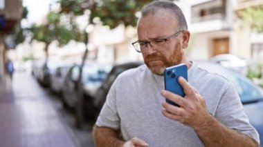 Yakışıklı, sakallı, orta yaşlı, beyaz bir adam, bir dış telefon görüşmesine kendini kaptırmış, uzaklaşıyor, kalabalık şehir caddesini geride bırakıyor..