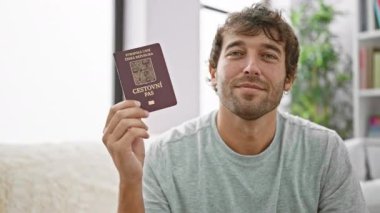 Oturma odasındaki kanepesinde oturan sakallı genç adam. Czech Cumhuriyet pasaportuyla sırıtıyor. Mutluluktan uçuyor, heyecanlı bir tatile çıkmaya hazır.