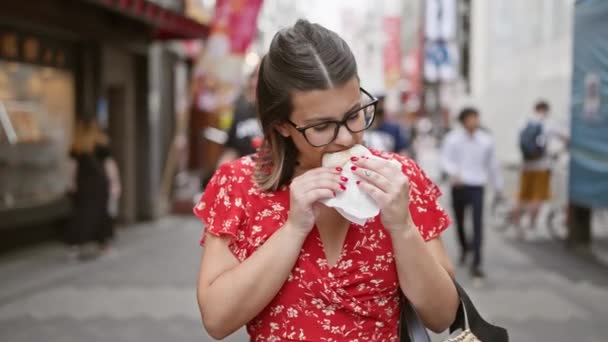美しいヒスパニックの女性は 大阪の有名なドトンボリ通りの美味しいカニ肉束を節約し 活気に満ちた街灯を反映した彼女の眼鏡 — ストック動画