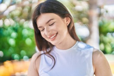 Beyaz bir kadın gülümsüyor parkın kenarına bakıyor.