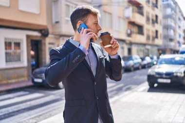 Young man business worker talking on smartphone drinking coffee at street