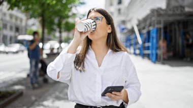 Akıllı telefon kullanan genç, güzel İspanyol kadın Madrid sokaklarında kahve içiyor.