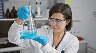 Kendine güveni tam ve genç İspanyol bir bilim adamı. Elinde bir test tüpü tutarken gülümsüyor. Laboratuvar ortamında yoğun çalışıyor..