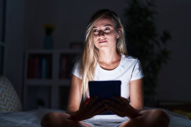 Yatak odasında dokunmatik ped kullanan genç sarışın kadın.