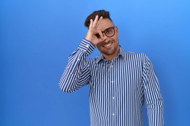 Sakallı, gözlüklü, el hareketleriyle gülümseyen, mutlu yüzüyle parmaklarının arasından bakan İspanyol bir adam.. 