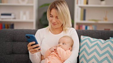 Anne ve kızı evde akıllı telefon kullanarak birbirlerine sarılıyorlar.