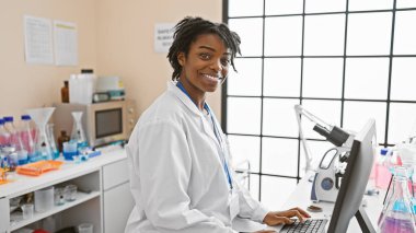 Tıbbi teçhizat ve mikroskopla çevrili bir laboratuvarda çalışan Afrikalı Amerikalı kadın bilim adamı..