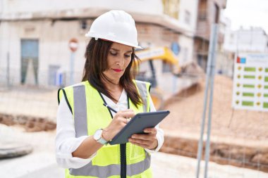 Young beautiful hispanic woman architect drawing on touchpad with relaxed expression at street