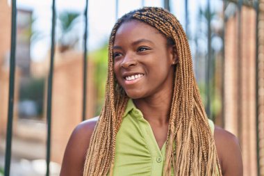 Afro-Amerikalı kadın gülümsüyor. Kendinden emin bir şekilde caddeye bakıyor.