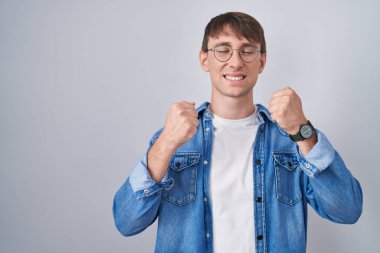 Başarı için heyecanlanan gözlüklü beyaz sarışın adam kollarını kaldırdı ve gözleri kapalı zaferi kutluyor. Kazanan konsept. 