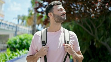 Sırt çantalı genç İspanyol turist parka gülümsüyor.