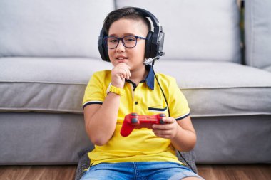 Elleri çenesinde kulaklık takmış video oyunu oynayan, soru soran, düşünceli bir çocuk. Gülümseyen ve düşünceli bir yüz. şüphe kavramı. 